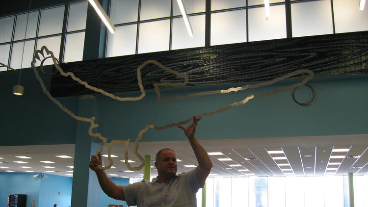 Miami artist Xavier Cortada displays a metallic pelican - the final piece of his new "Pelican Path" artwork installed in Cruise Terminal 4 at Port Everglades. The bird now hangs from the terminal ceiling in front of a mural of colorful water ripples created from porcelain tiles. (Arlene Satchell / Sun Sentinel)